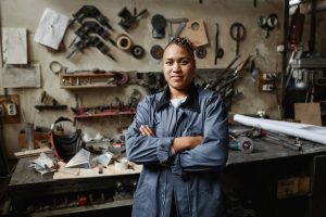 Waist up portrait of multiethnic female worker posing in workshop with arms crossed and looking at camera, copy space